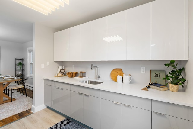 kitchen featuring a baseboard heating unit, white cabinetry, sink, and light hardwood / wood-style flooring