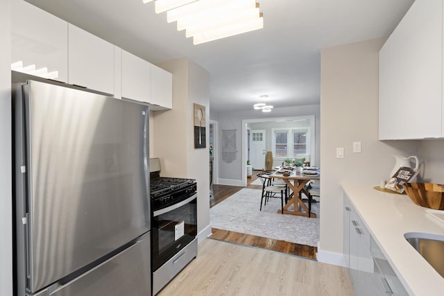 kitchen with stainless steel appliances, white cabinetry, and light hardwood / wood-style flooring