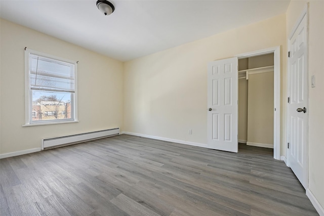 unfurnished bedroom with wood-type flooring and a baseboard heating unit