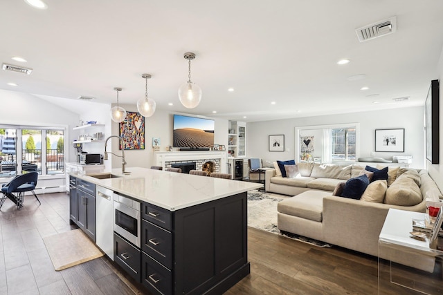 kitchen with sink, stainless steel microwave, dark hardwood / wood-style floors, pendant lighting, and a kitchen island with sink