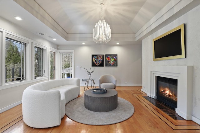 living area featuring a tray ceiling, visible vents, baseboards, and wood finished floors