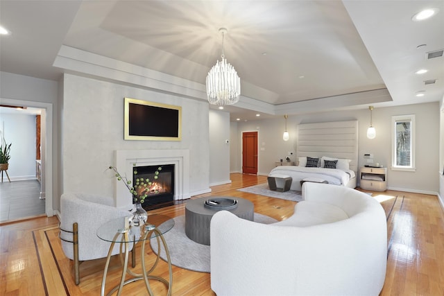 living area with recessed lighting, a raised ceiling, light wood-style floors, a glass covered fireplace, and baseboards