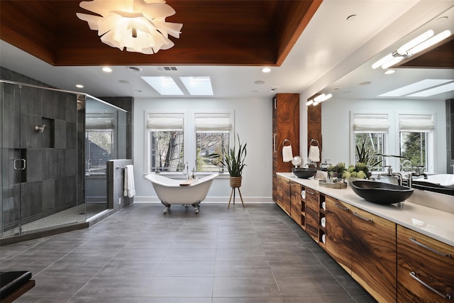 full bathroom with a skylight, baseboards, a soaking tub, a shower stall, and double vanity