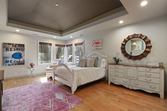 bedroom featuring baseboards, a tray ceiling, light wood-style flooring, and recessed lighting