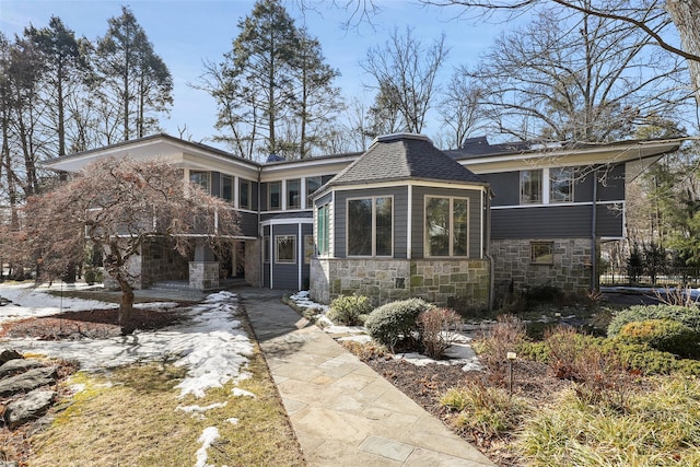 view of front of home featuring a sunroom, stone siding, a shingled roof, and a chimney