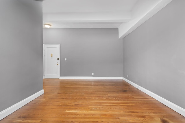 spare room with beamed ceiling and light hardwood / wood-style floors