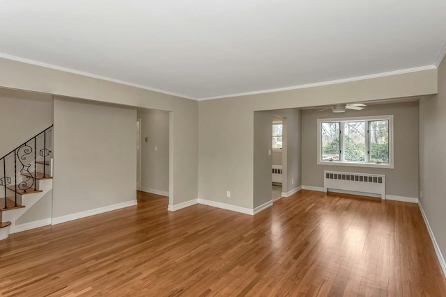 empty room with radiator, stairway, baseboards, and wood finished floors