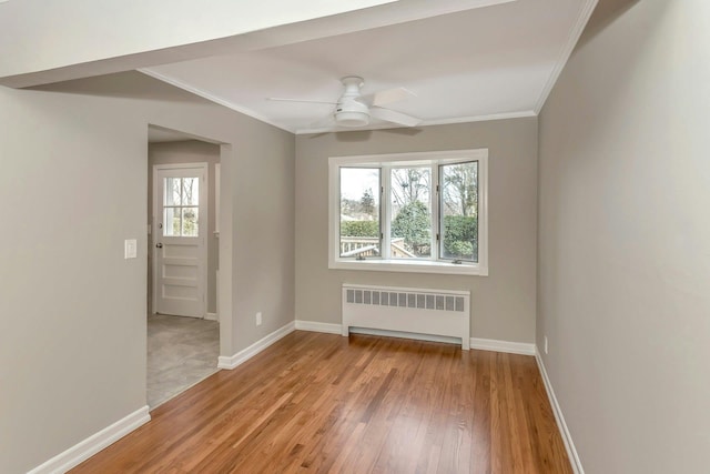 empty room featuring light wood-style floors, radiator, crown molding, and baseboards