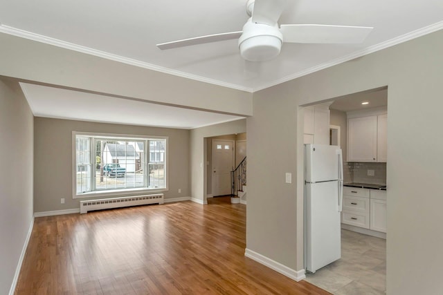 spare room featuring light wood finished floors, baseboards, a ceiling fan, baseboard heating, and crown molding