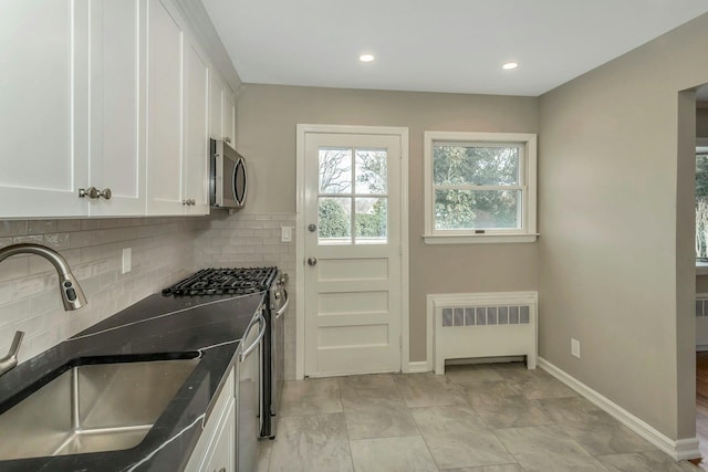 kitchen featuring decorative backsplash, white cabinets, radiator, stainless steel appliances, and a sink