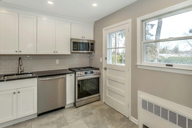 kitchen with white cabinets, dark countertops, radiator heating unit, stainless steel appliances, and a sink