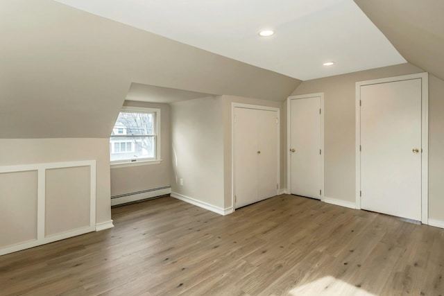 additional living space with lofted ceiling, light wood finished floors, baseboards, and a baseboard heating unit