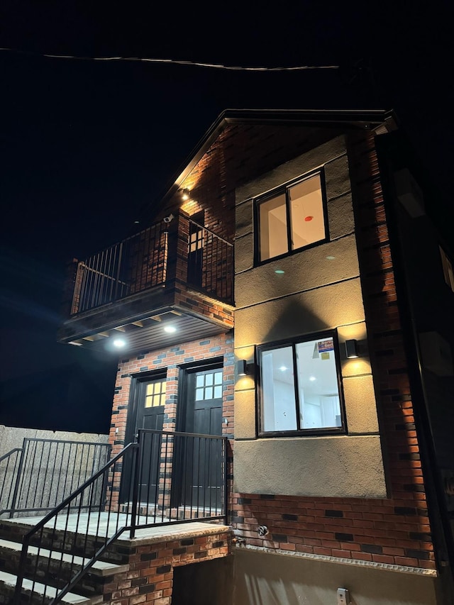 exterior entry at twilight with a balcony, brick siding, and stucco siding