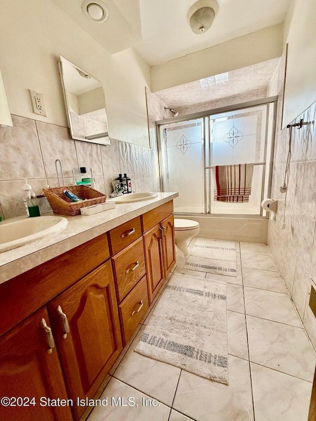 full bathroom with tile walls, vanity, toilet, and combined bath / shower with glass door