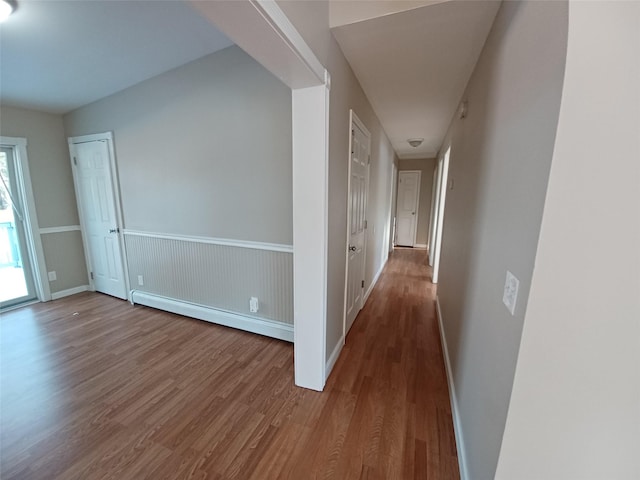 corridor with wood-type flooring and baseboard heating