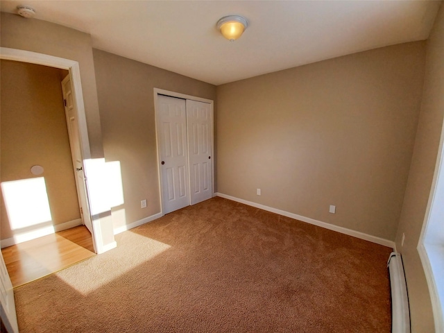 unfurnished bedroom featuring baseboard heating, light colored carpet, and a closet