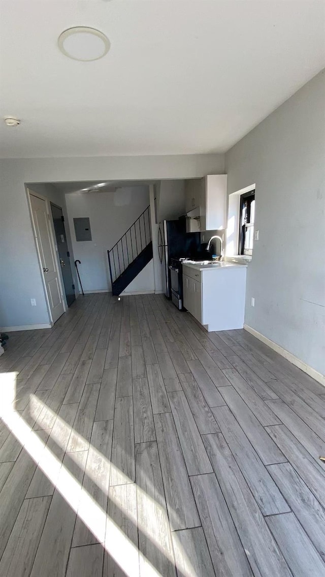 kitchen featuring light wood finished floors, white cabinets, baseboards, and gas range oven