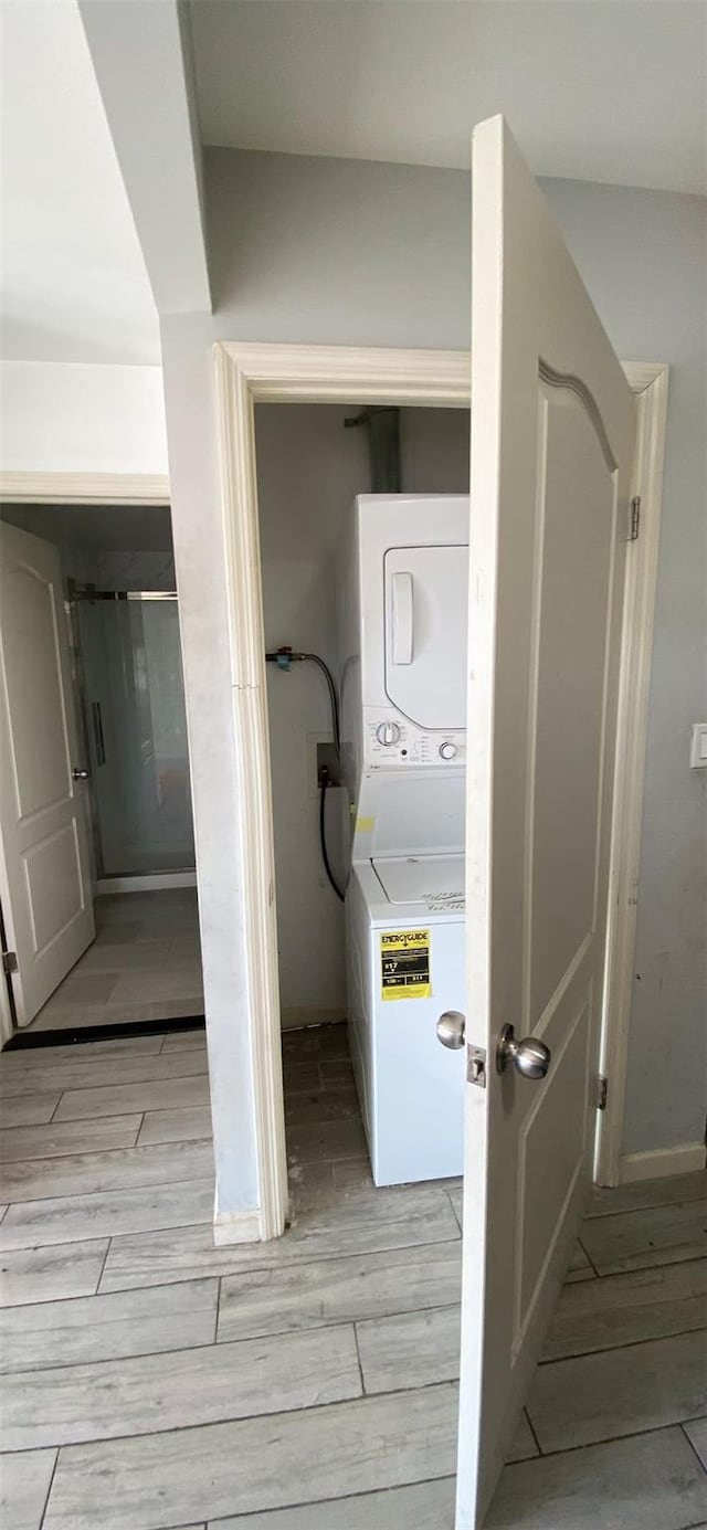 clothes washing area featuring wood tiled floor, laundry area, and stacked washing maching and dryer