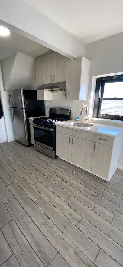 kitchen featuring under cabinet range hood, gas stove, light wood-type flooring, and a sink