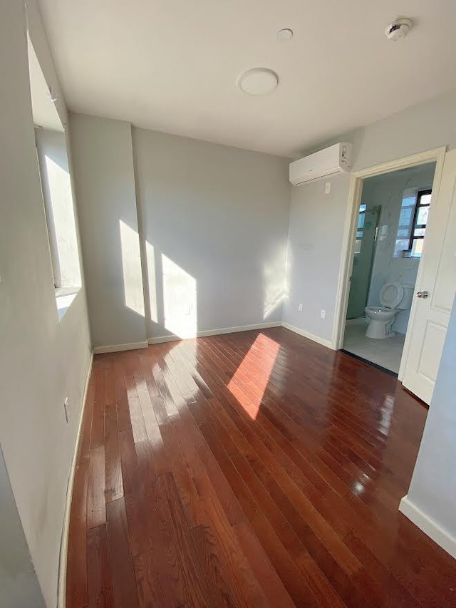 spare room featuring hardwood / wood-style floors, an AC wall unit, and baseboards