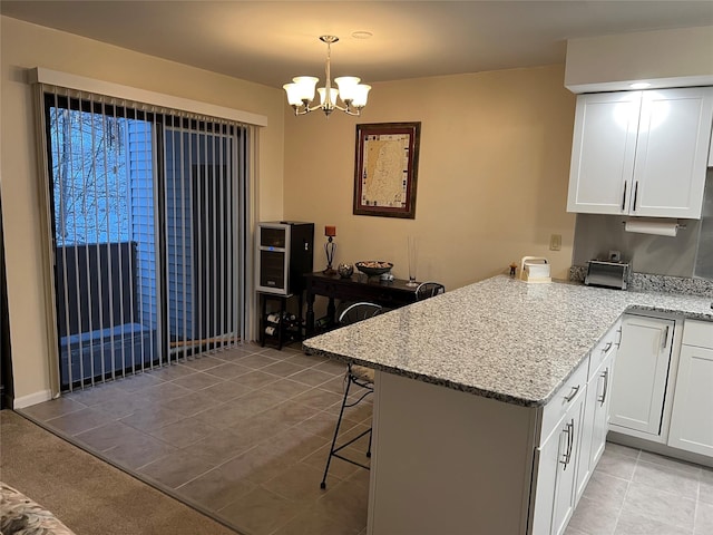 kitchen featuring a notable chandelier, a peninsula, a breakfast bar, and white cabinets