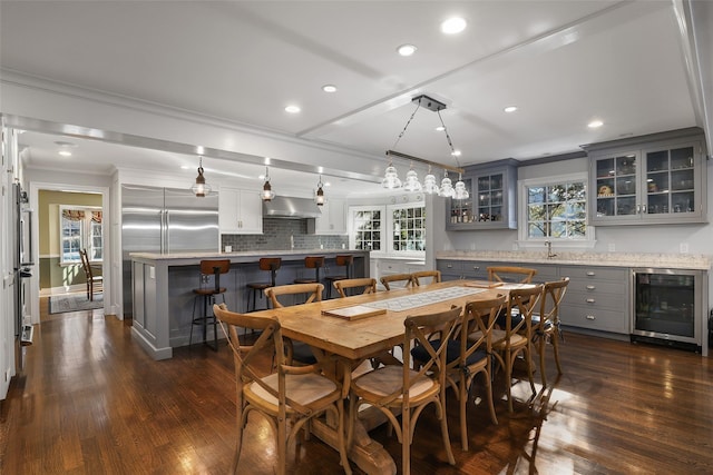 dining area featuring dark wood-type flooring, ornamental molding, beverage cooler, and indoor bar