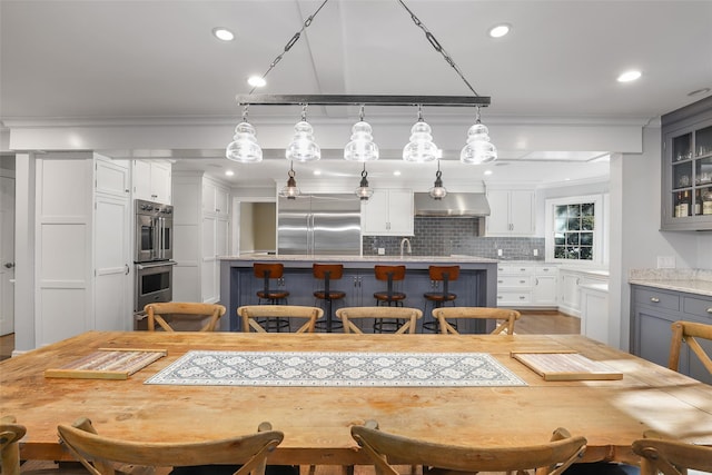 kitchen with a breakfast bar, gray cabinetry, decorative light fixtures, ventilation hood, and appliances with stainless steel finishes