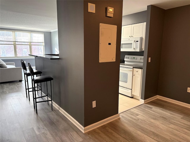 kitchen with white appliances, electric panel, light wood-type flooring, and white cabinets