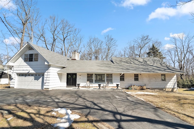 view of front of house with a garage, roof with shingles, driveway, and a chimney