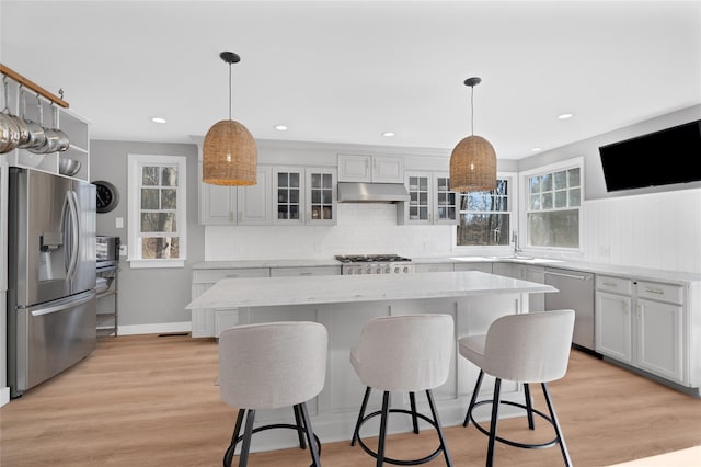 kitchen with under cabinet range hood, a kitchen bar, appliances with stainless steel finishes, and light wood-style floors