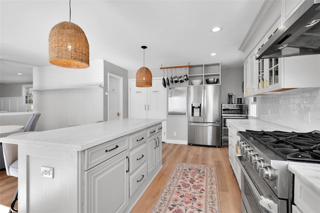 kitchen featuring light wood finished floors, backsplash, appliances with stainless steel finishes, white cabinetry, and extractor fan