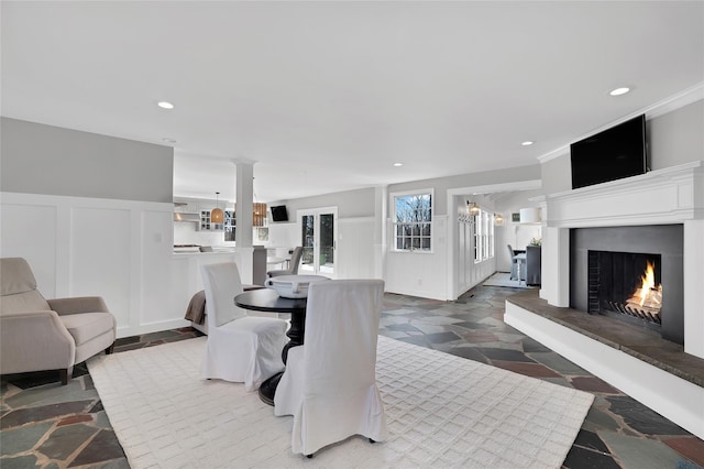 dining area with recessed lighting, a decorative wall, stone finish flooring, wainscoting, and a lit fireplace