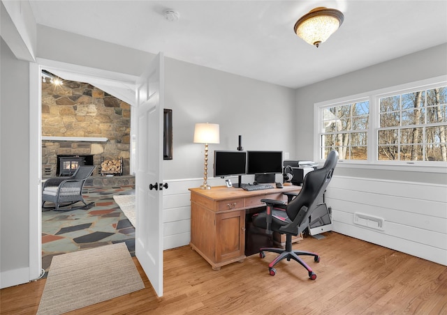 office featuring light wood-style flooring, a stone fireplace, and wainscoting