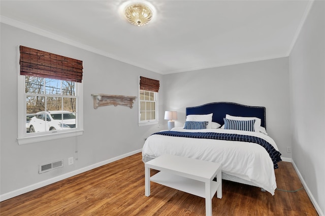 bedroom with ornamental molding, wood finished floors, visible vents, and baseboards