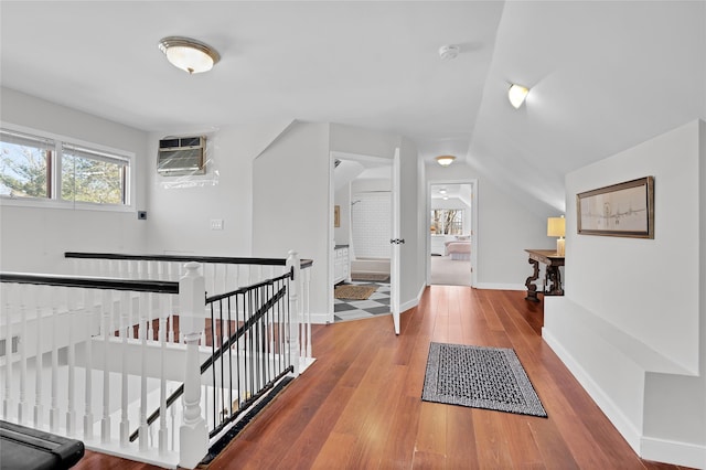 hallway featuring wood-type flooring, baseboards, an AC wall unit, and an upstairs landing