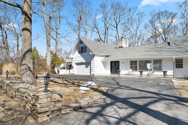 view of front of home with a garage, roof with shingles, driveway, and a chimney