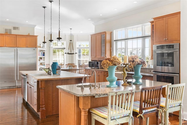 kitchen featuring appliances with stainless steel finishes, dark hardwood / wood-style floors, decorative light fixtures, an island with sink, and ornamental molding