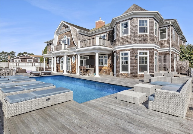 rear view of property featuring a pool with hot tub, outdoor lounge area, and a balcony