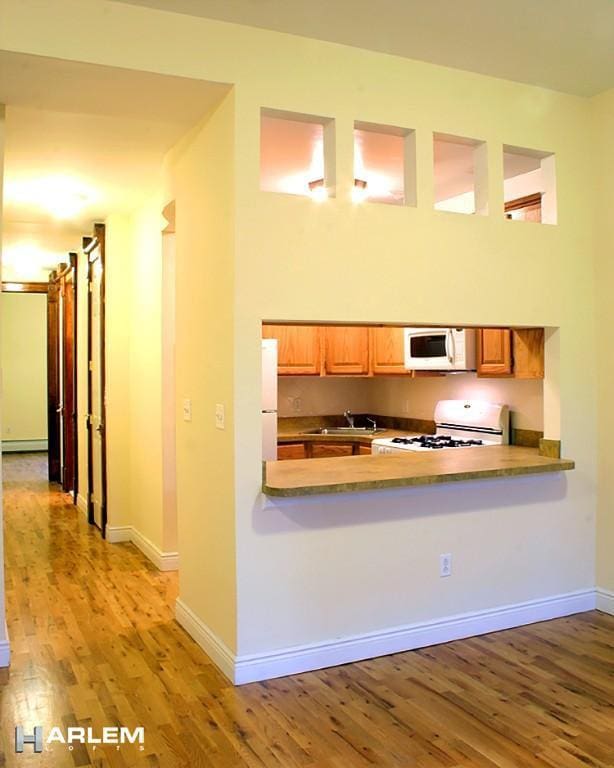 kitchen featuring sink, a high ceiling, light hardwood / wood-style floors, kitchen peninsula, and white appliances