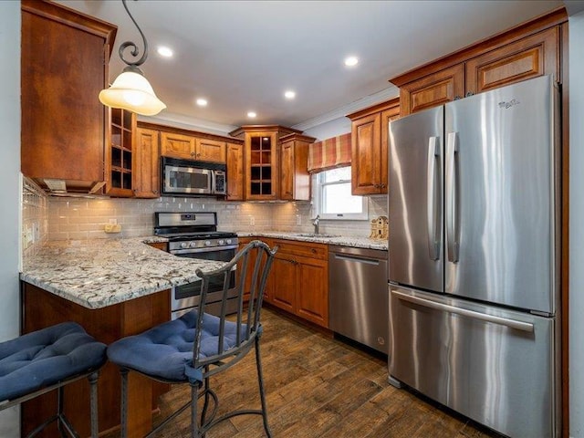 kitchen featuring appliances with stainless steel finishes, decorative light fixtures, sink, a kitchen breakfast bar, and light stone countertops