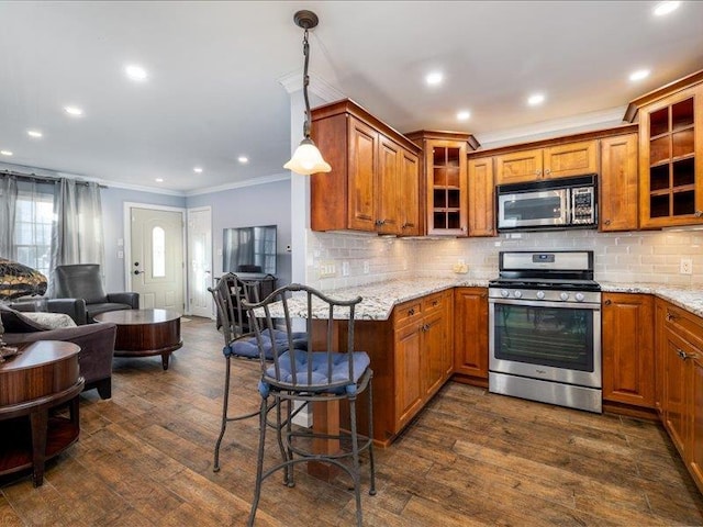 kitchen with appliances with stainless steel finishes, hanging light fixtures, dark hardwood / wood-style floors, light stone counters, and ornamental molding