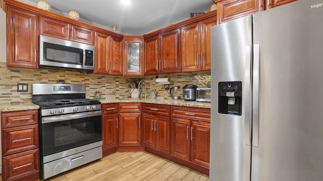 kitchen featuring stainless steel appliances, light stone countertops, backsplash, and light hardwood / wood-style flooring