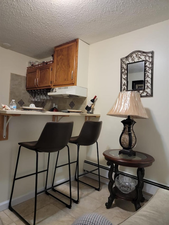 kitchen featuring a kitchen bar, kitchen peninsula, decorative backsplash, and a textured ceiling