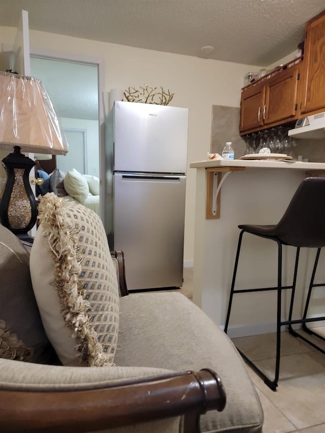 interior space featuring light tile patterned floors, stainless steel refrigerator, tasteful backsplash, a textured ceiling, and a kitchen bar