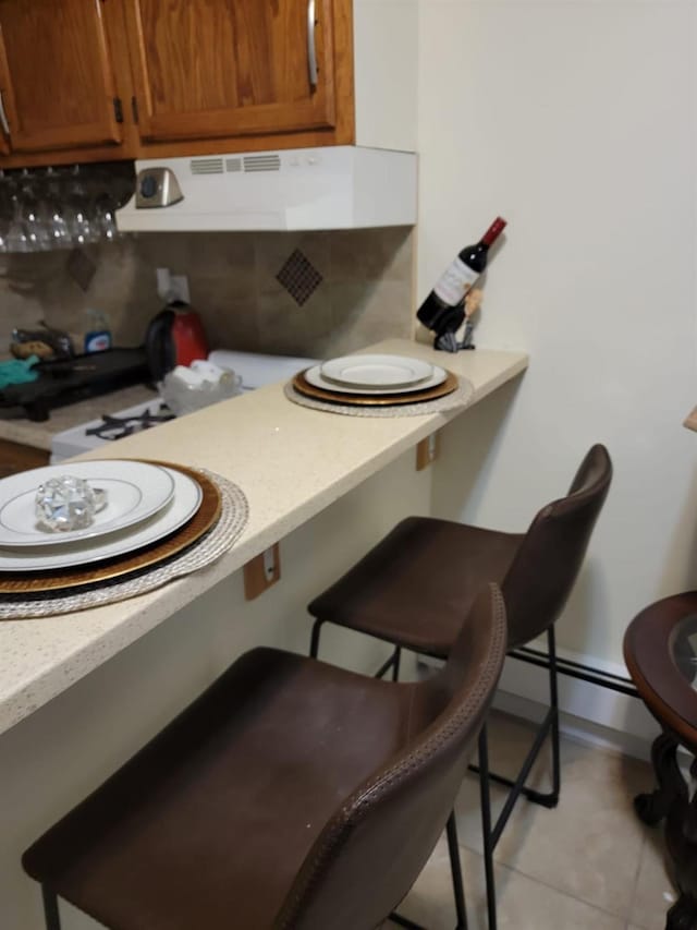 kitchen featuring light tile patterned flooring, ventilation hood, a kitchen bar, decorative backsplash, and a baseboard heating unit