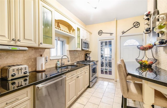 kitchen with sink, dark stone counters, light tile patterned floors, stainless steel appliances, and cream cabinets