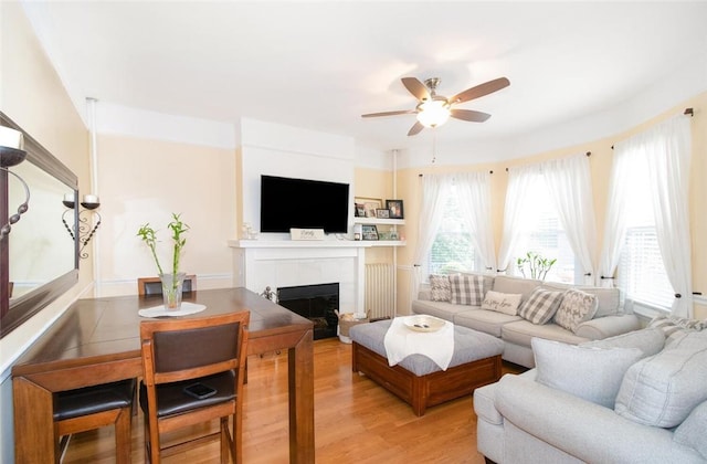 living room with a tile fireplace, ceiling fan, and light hardwood / wood-style flooring