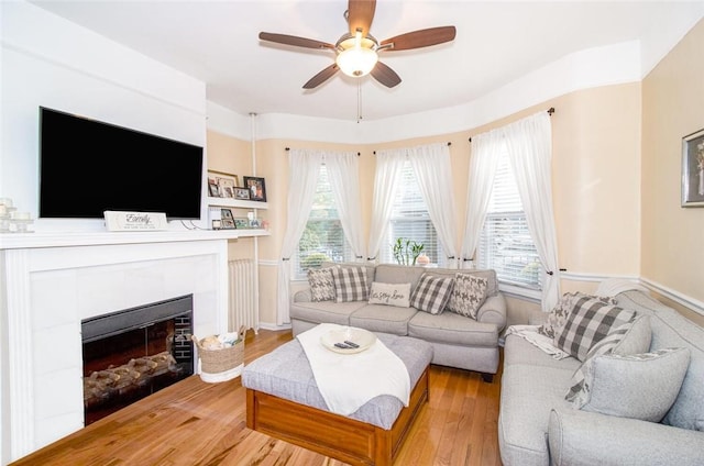 living room with a tile fireplace, ceiling fan, and light wood-type flooring