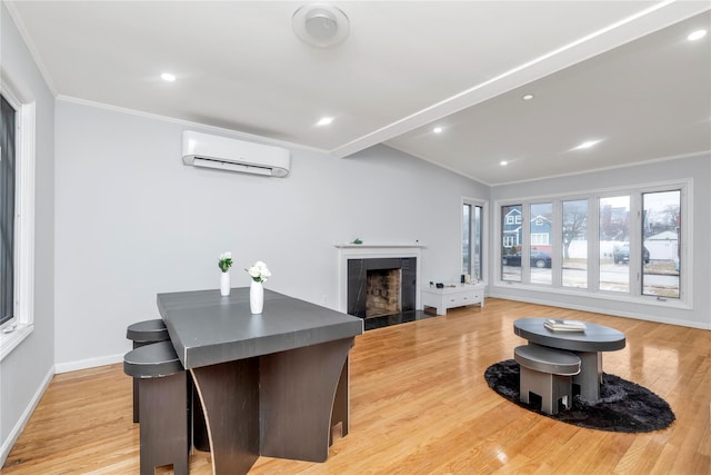 dining space with a wall mounted air conditioner, crown molding, a fireplace, and light wood-type flooring