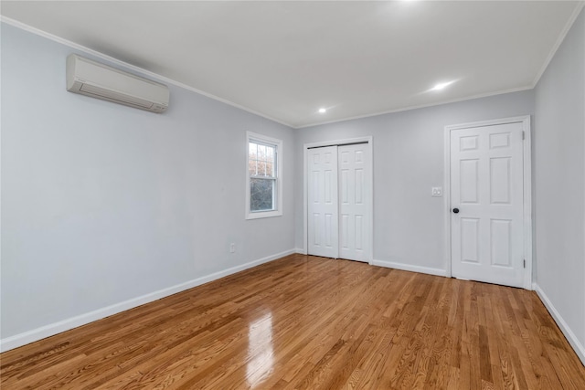 unfurnished bedroom with ornamental molding, a wall mounted air conditioner, a closet, and light hardwood / wood-style flooring